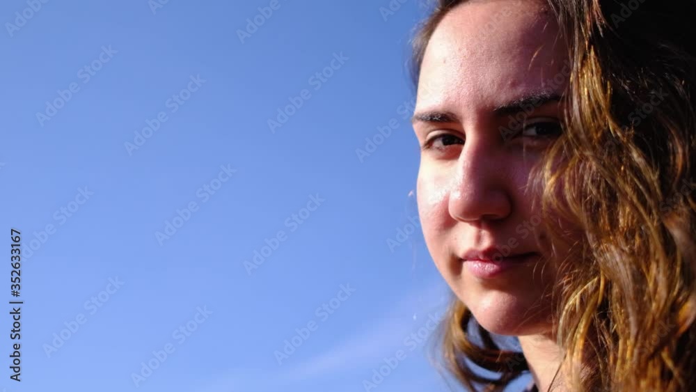 Closeup side view of young pretty caucasian girl looking at camera with sky background. Auburn young teenager and cloudless sky Closeup side view of young pretty caucasian girl looking at camera with sky background. Auburn young teenager and cloudless sky