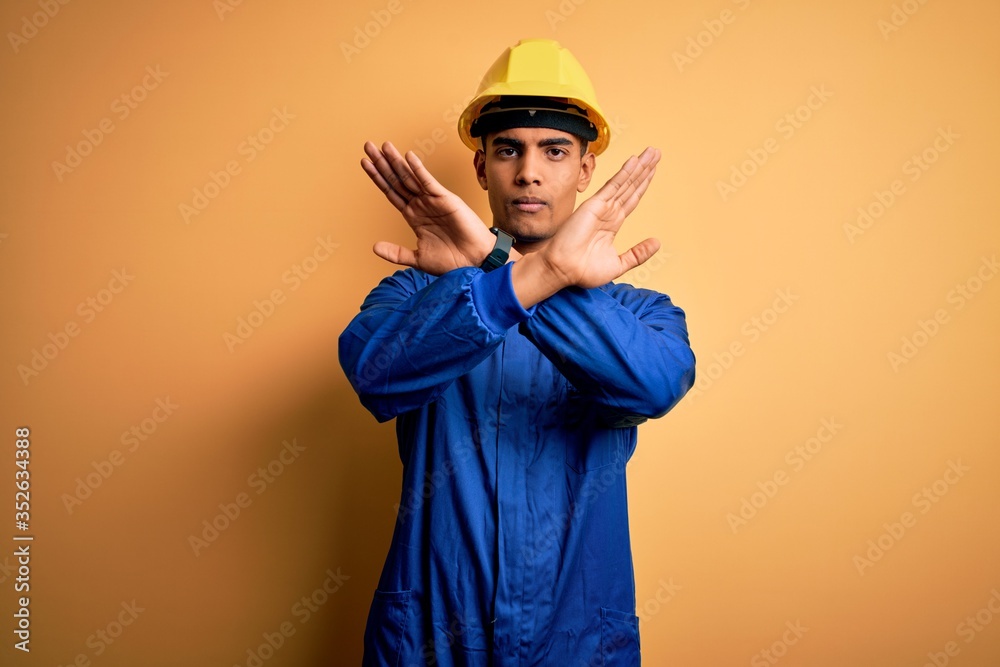 Young handsome african american worker man wearing blue uniform and security helmet Rejection expression crossing arms doing negative sign, angry face