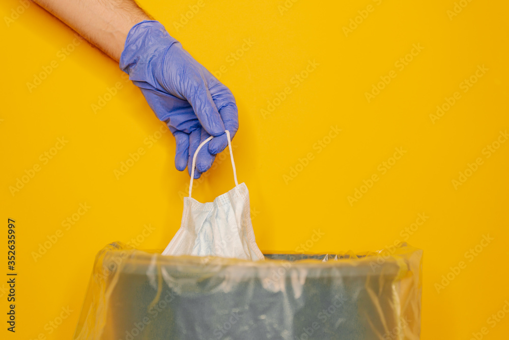 The blue latex gloved hand putting the surgical mask in the trash The blue latex gloved hand putting the surgical mask in the trash