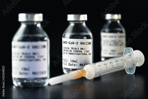 Coronavirus Covid-19 vaccine concept - three glass vials on black table, hypodermic syringe near closeup detail (label own design - dummy data, not real product)