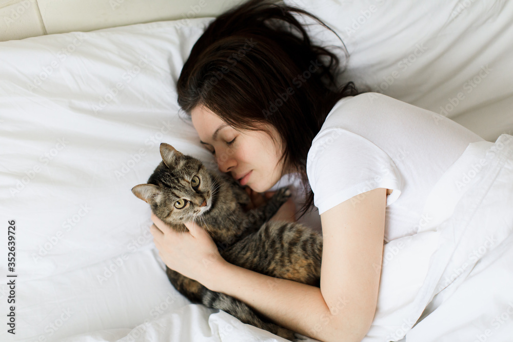 beautiful smiling girl with eyes closed lying in bed and hugging cat