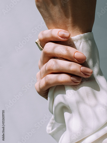 Close up minimalistic beige manicure in the sun. Concept of health, beautiful skin of hands and manicure. Body care and and dermatology.