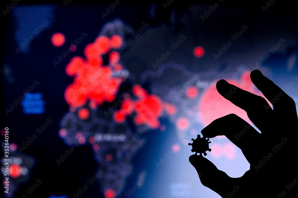 Hands silhouette holds covid 19 virus. World map of coronavirus in background
