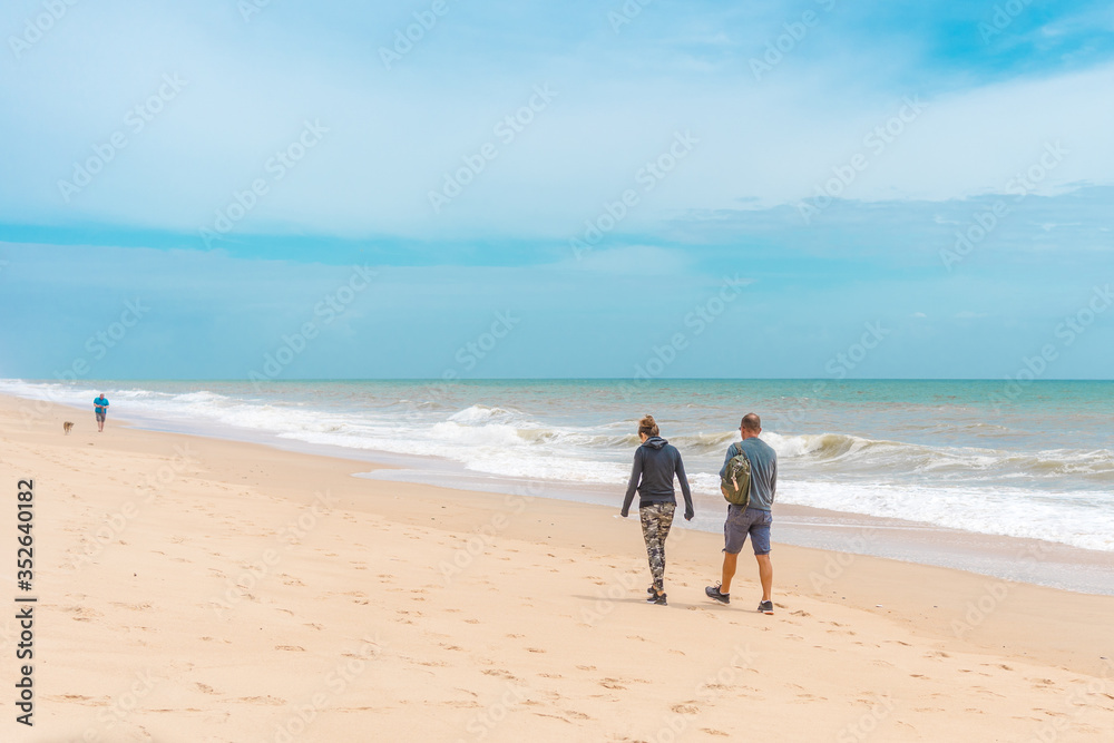 Back view of people walking on a beautiful deserted beach natural seascape cloudy sky landscape outdoors background.