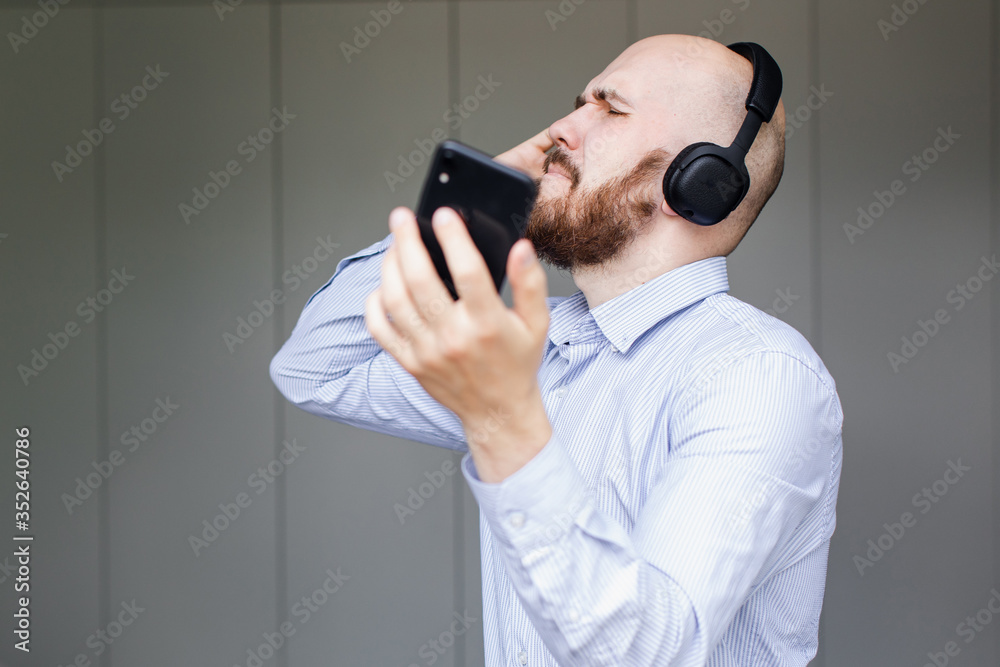 Naklejka premium a bearded bald man sings songs and listens to music with headphones at home