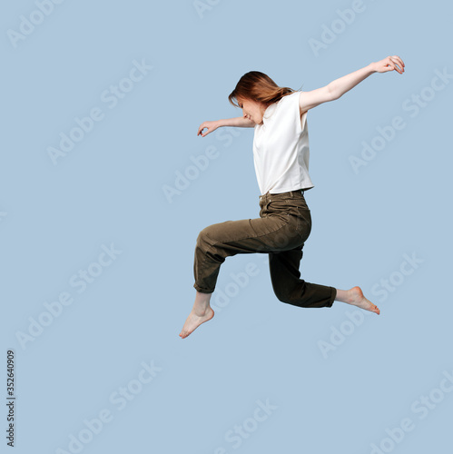Young woman doing figure jump over blue background.
