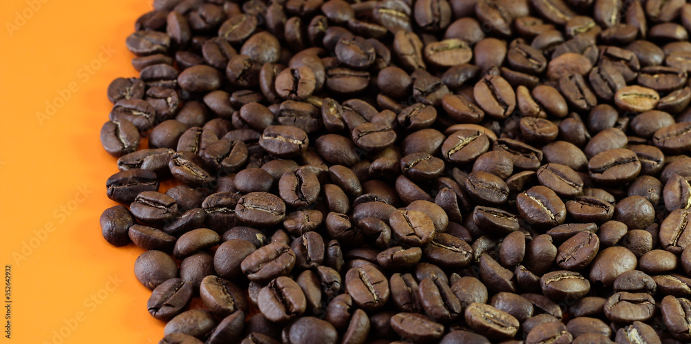 Fototapeta premium Coffee beans on a bright background. Coffee granules on an orange table. Texture of coffee beans.