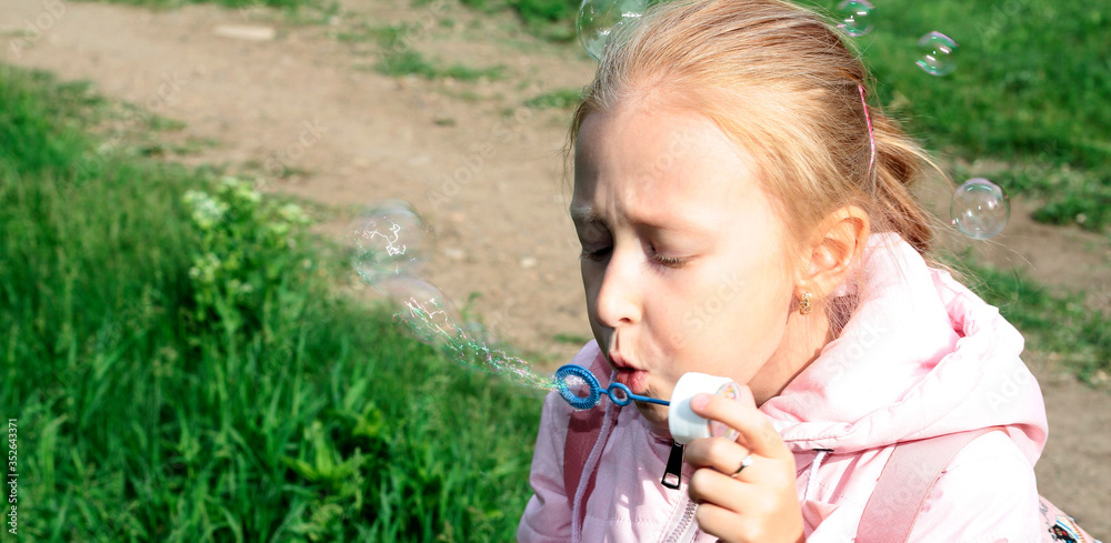 A girl plays with soap bubbles. A child blows a soap bubble in the open air. Child's play.