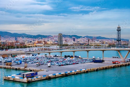 Barcelona, Spain. Porta d’Europa bascule bridge over Barcelona Port and Wharfs, with Torre Jaume I aerial lift steel truss tower, mountains, city skyline architecture in background.