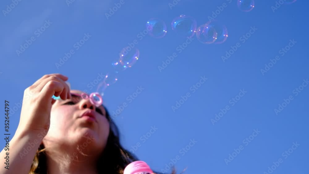 Young woman blowing soap bubbles towards the sky in slow motion. Bottom view of pretty auburn woman blowing soap bubbles on the roof Young woman blowing soap bubbles towards the sky in slow motion. Bottom view of pretty auburn woman blowing soap bubbles on the roof