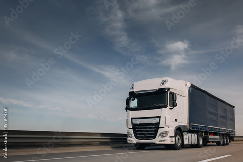 Semi-truck with cargo trailer driving at the city streets. Fast moving truck. Lorry truck driver go fast at the empty autobahn. Express and logistic delivery service
