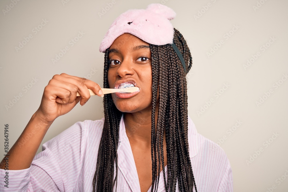 Young beautiful african american woman wearing pajama and sleep mask brushing her teeth using tooth brush and oral paste, cleaning teeth and tongue as healthy health care morning routine Young beautiful african american woman wearing pajama and sleep mask brushing her teeth using tooth brush and oral paste, cleaning teeth and tongue as healthy health care morning routine