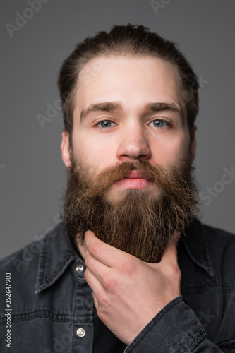 Portrait of thinking stylish young man touch his beard isolated on gray background