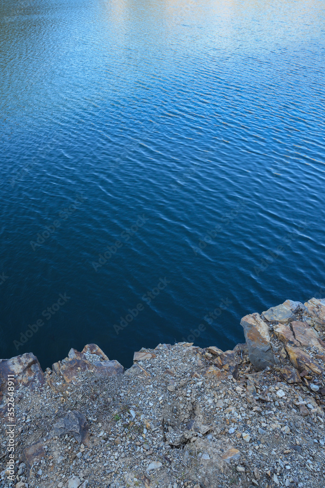 Obraz premium Stone rocks near water, on the background of lake, river, sea, ocean. Blue clear water. Artificial reservoirs