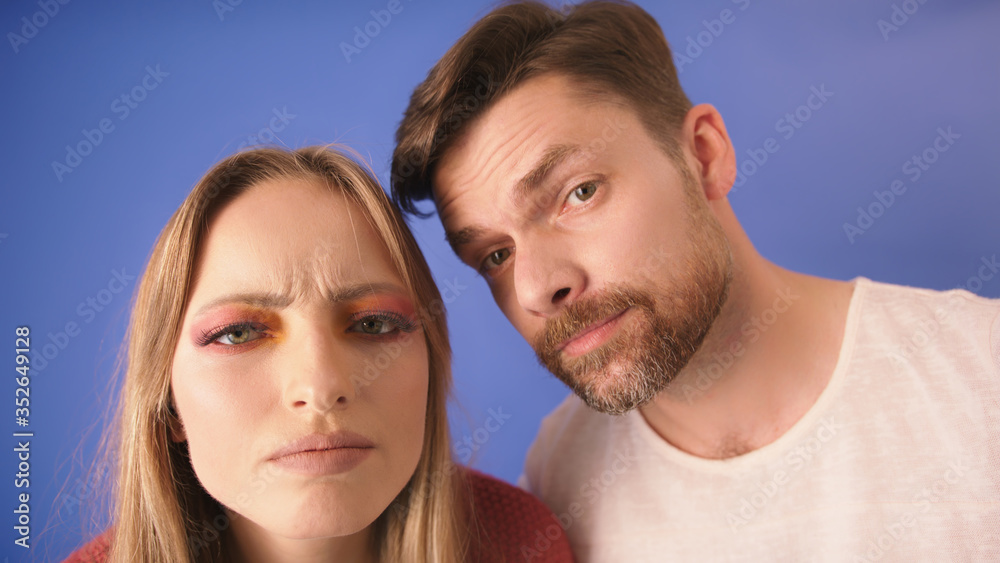 Young couple looking confused into the camera. Isolated on the blue background. Face expressions. Young couple looking confused into the camera. Isolated on the blue background. Face expressions.
