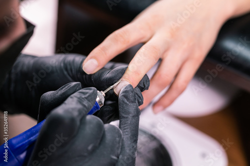 Manicurist use electric nail file drill in beauty salon. Perfect nails manicure process close up with burst flying debris.