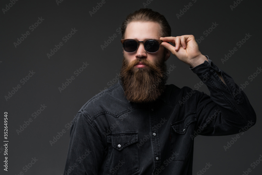 Fototapeta premium Portrait of handsome s bearded young man with serious expression wearing sunglasses over gray background