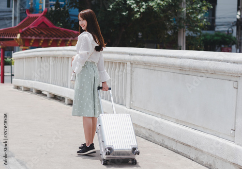 Beautiful traveler asian woman wearing white shirt, long skirt and hat with large luggage on white bridge background in Bangkok city Thailand, travel concept.