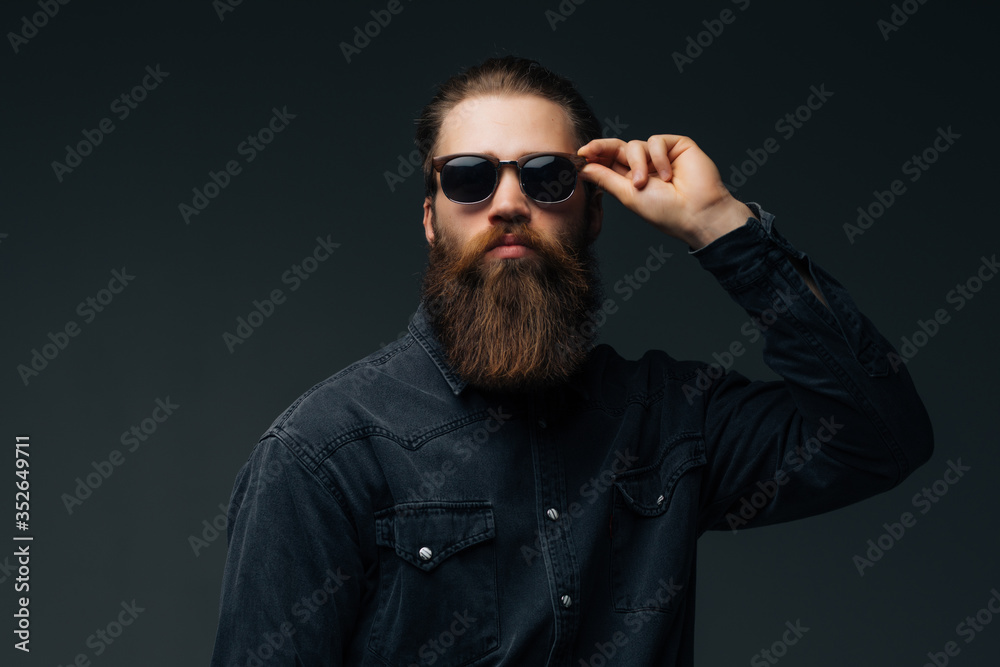 Fototapeta premium Portrait of handsome s bearded young man with serious expression wearing sunglasses over gray background