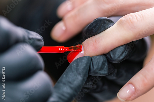 Close Up shot of master in rubber gloves covering red nails with top coat in the beauty salon. Perfect nails manicure process.