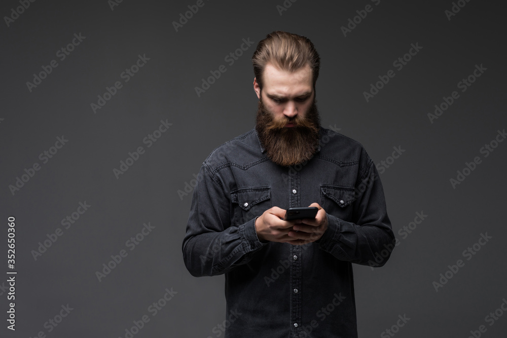 Portrait of a handsome attractive long bearded man holding mobile phone isolated on gray background Portrait of a handsome attractive long bearded man holding mobile phone isolated on gray background