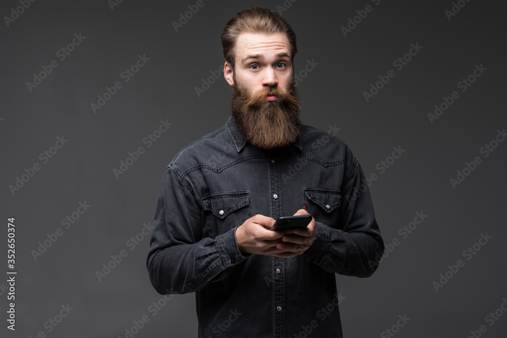 Portrait of a handsome attractive long bearded man holding mobile phone isolated on gray background Portrait of a handsome attractive long bearded man holding mobile phone isolated on gray background