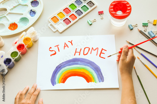 Girl painting rainbow on paper during Covid-19 quarantine at home. Stay home