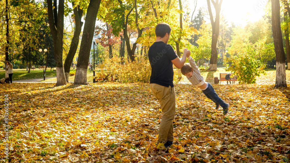 Young father holding his son by hands and spinning in autumn park Young father holding his son by hands and spinning in autumn park