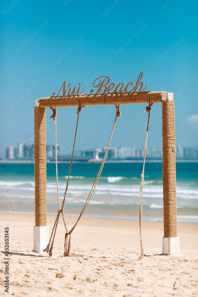 Wooden square arch on sandy beach near blue sea with blur background of big city life. Beautiful place to relax. Concept of travelling and vacation. Wooden square arch on sandy beach near blue sea with blur background of big city life. Beautiful place to relax. Concept of travelling and vacation.