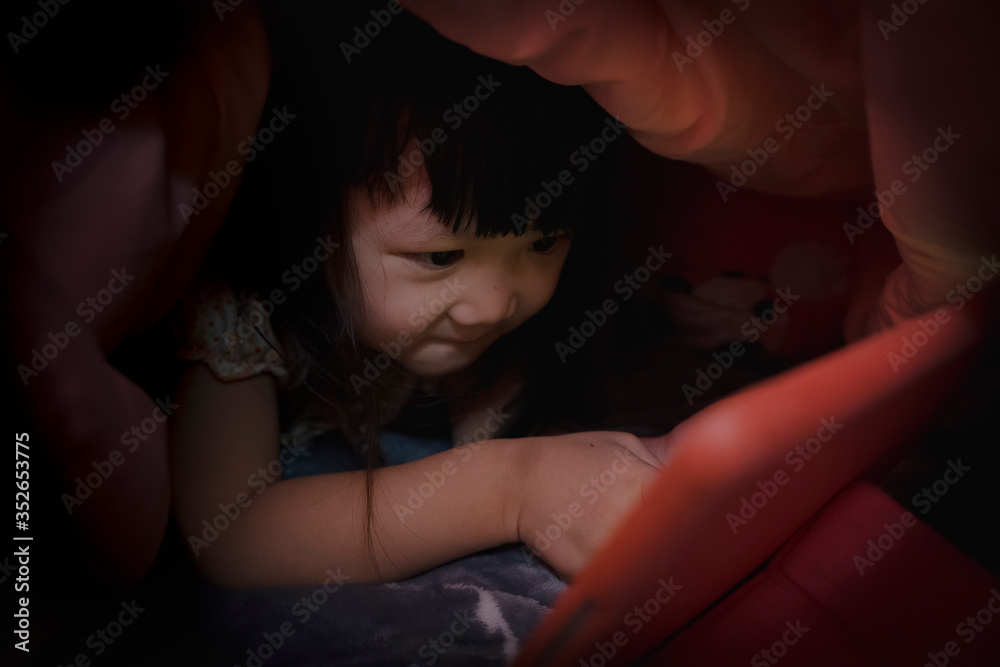 Cute little girl with tablet computer watching cartoons under blanket Cute little girl with tablet computer watching cartoons under blanket