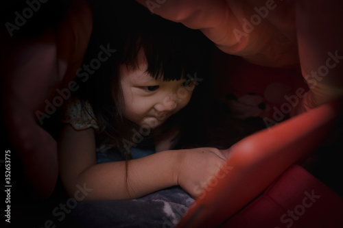 Cute little girl with tablet computer watching cartoons under blanket