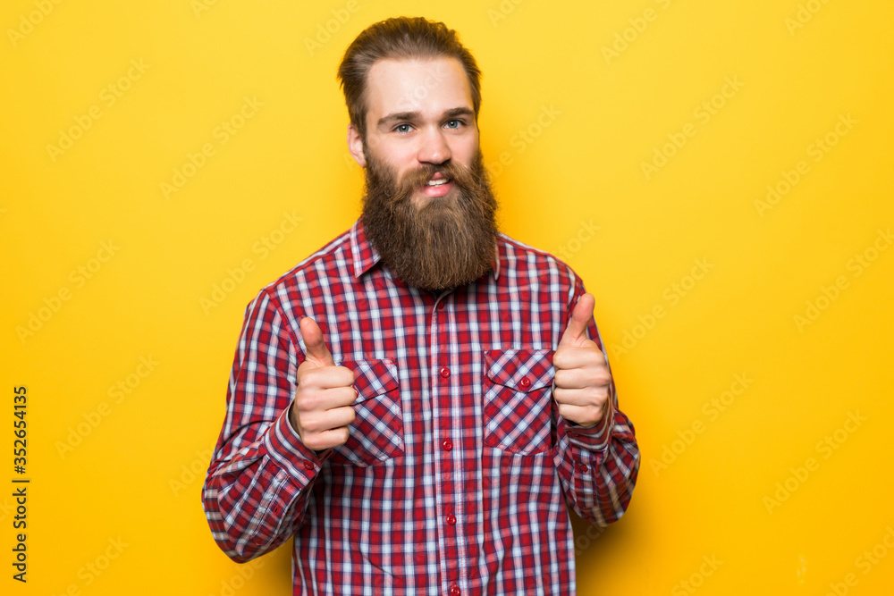 Fototapeta premium Young bearded man with thumbs up on yellow background