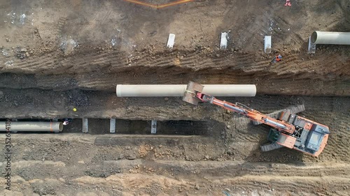 Concrete pipe tube installation. Aerial above men at work outside with heavy machinery to connect and install water or sewerage pipeline in a digging soil land