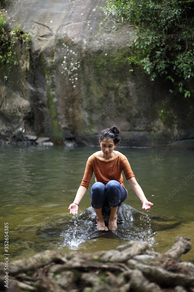Woman sitting on a rock at a waterfall Woman sitting on a rock at a waterfall