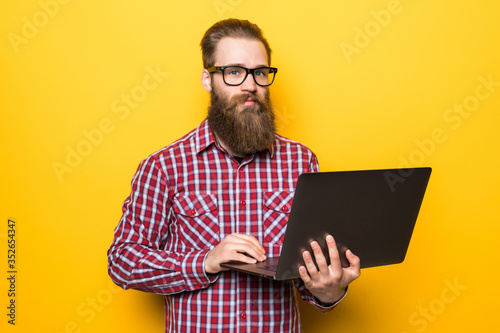 Young bearded man with laptop on yellow background