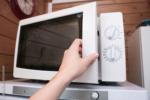 Woman hand opening microwave oven in order to prepare, heat food for lunch or dinner, kitchen elecrtric appliances using concept photo