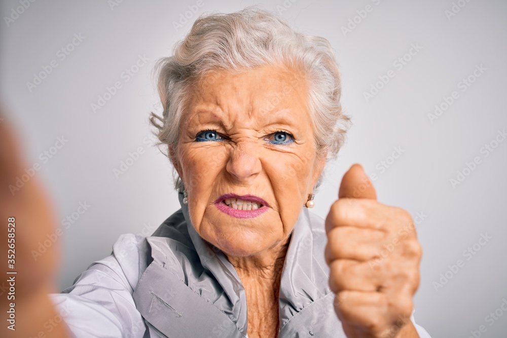 Senior beautiful grey-haired woman making selfie by camera over isolated white background annoyed and frustrated shouting with anger, crazy and yelling with raised hand, anger concept Senior beautiful grey-haired woman making selfie by camera over isolated white background annoyed and frustrated shouting with anger, crazy and yelling with raised hand, anger concept