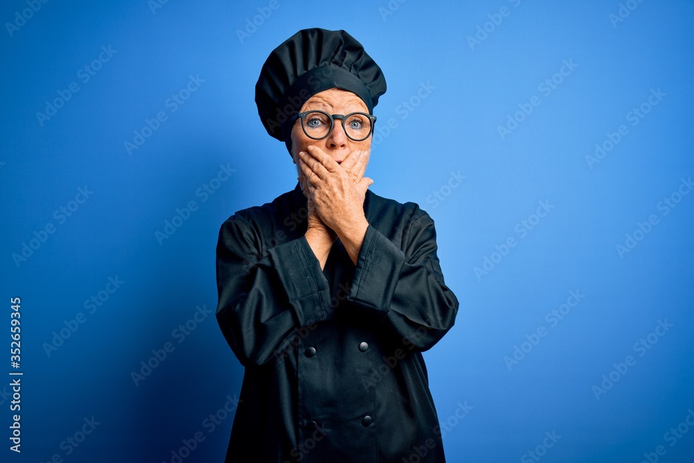 Senior beautiful grey-haired chef woman wearing cooker uniform and hat over blue background shocked covering mouth with hands for mistake. Secret concept. Senior beautiful grey-haired chef woman wearing cooker uniform and hat over blue background shocked covering mouth with hands for mistake. Secret concept.