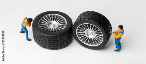 The concept of the workshop tire fitting. Miniature mechanics repairing toy car wheel, close up.