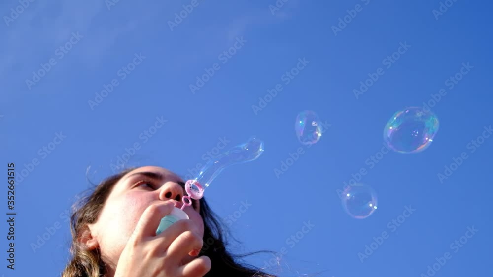 Young woman blowing soap bubbles towards the sky in slow motion. Bottom view of pretty auburn woman blowing soap bubbles on the roof Young woman blowing soap bubbles towards the sky in slow motion. Bottom view of pretty auburn woman blowing soap bubbles on the roof