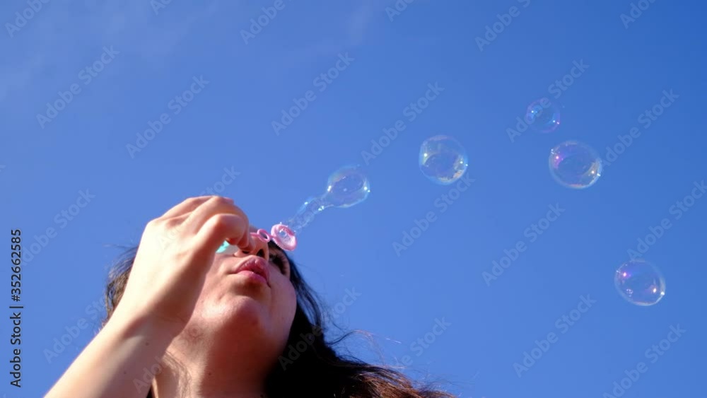 Young woman blowing soap bubbles towards the sky in slow motion. Bottom view of pretty auburn woman blowing soap bubbles on the roof Young woman blowing soap bubbles towards the sky in slow motion. Bottom view of pretty auburn woman blowing soap bubbles on the roof