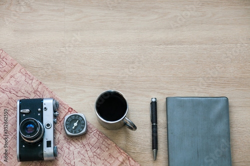 Vintage Photo Camera, Note Book, Compass, Pen, Metal Coffee Cup, Map on The Wooden Background 