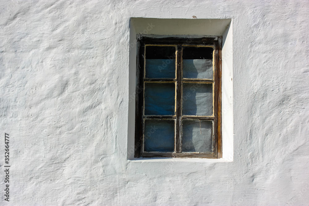An old window against the background of a white clay house in the village in summer.