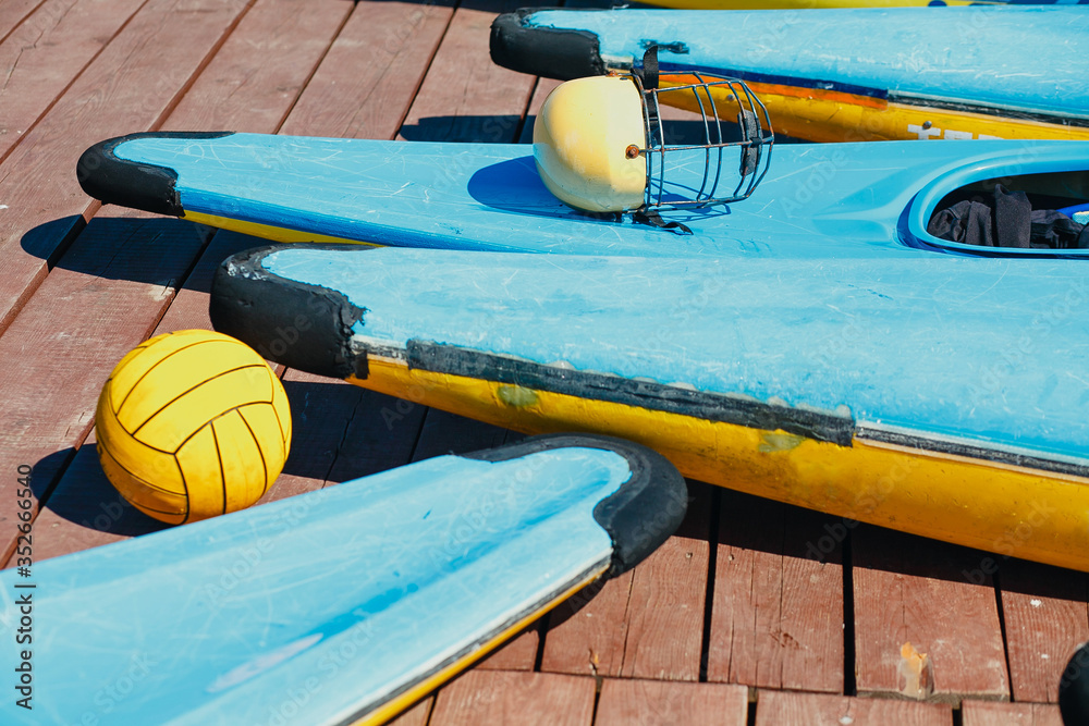 colored kayaks, ball and helmet on a wooden pier colored kayaks, ball and helmet on a wooden pier