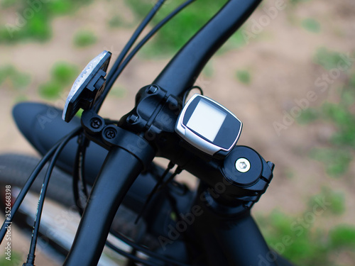 Bicycle speedometer on handlebar on blurred forest background. © Alexey