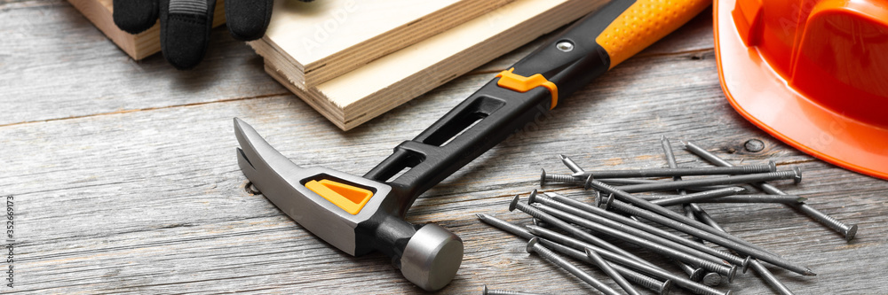 Carpentry tools hammer, nails, wooden bars, helmet and gloves on a gray wooden table. Banner	