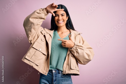 Young beautiful hispanic fashion woman wearing winter jacket and sweater over pink background smiling making frame with hands and fingers with happy face. Creativity and photography concept.