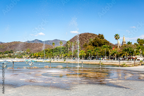 Fountain spraying the ground with jets of water on the promenade of Lake Chapala with the town in the background, sunny day with a clear blue sky in Jalisco, Mexico photo