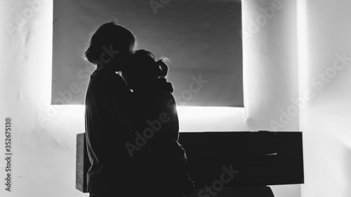 Two people hugging each other before a coffin in a lonely, sad room. They might be in a funeral, burial, hospital, church or waiting for cremation. Black and white mourning, grief, sorrow & death.