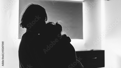 Two people hugging each other before a coffin in a lonely, sad room. They might be in a funeral, burial, hospital, church or waiting for cremation. Black and white mourning, grief, sorrow & death.